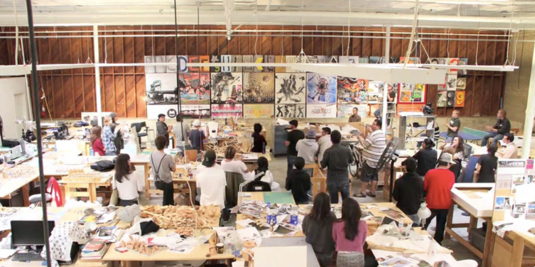 Image of an open, academic architecture studio environment during a crit with large posters on the wall and students looking toward the posters